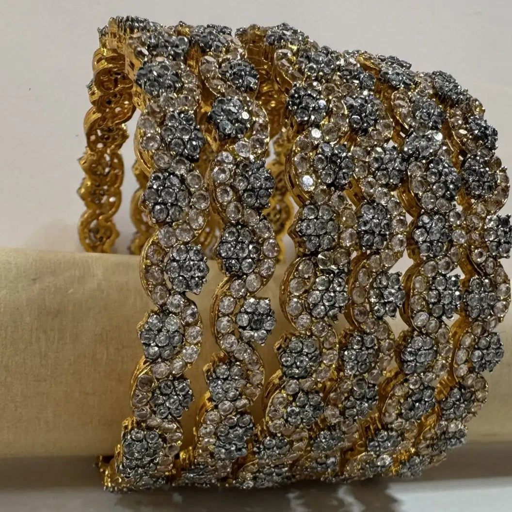 gold plated bangles with floral patterns with silver embellishments against a white surface and wood stick