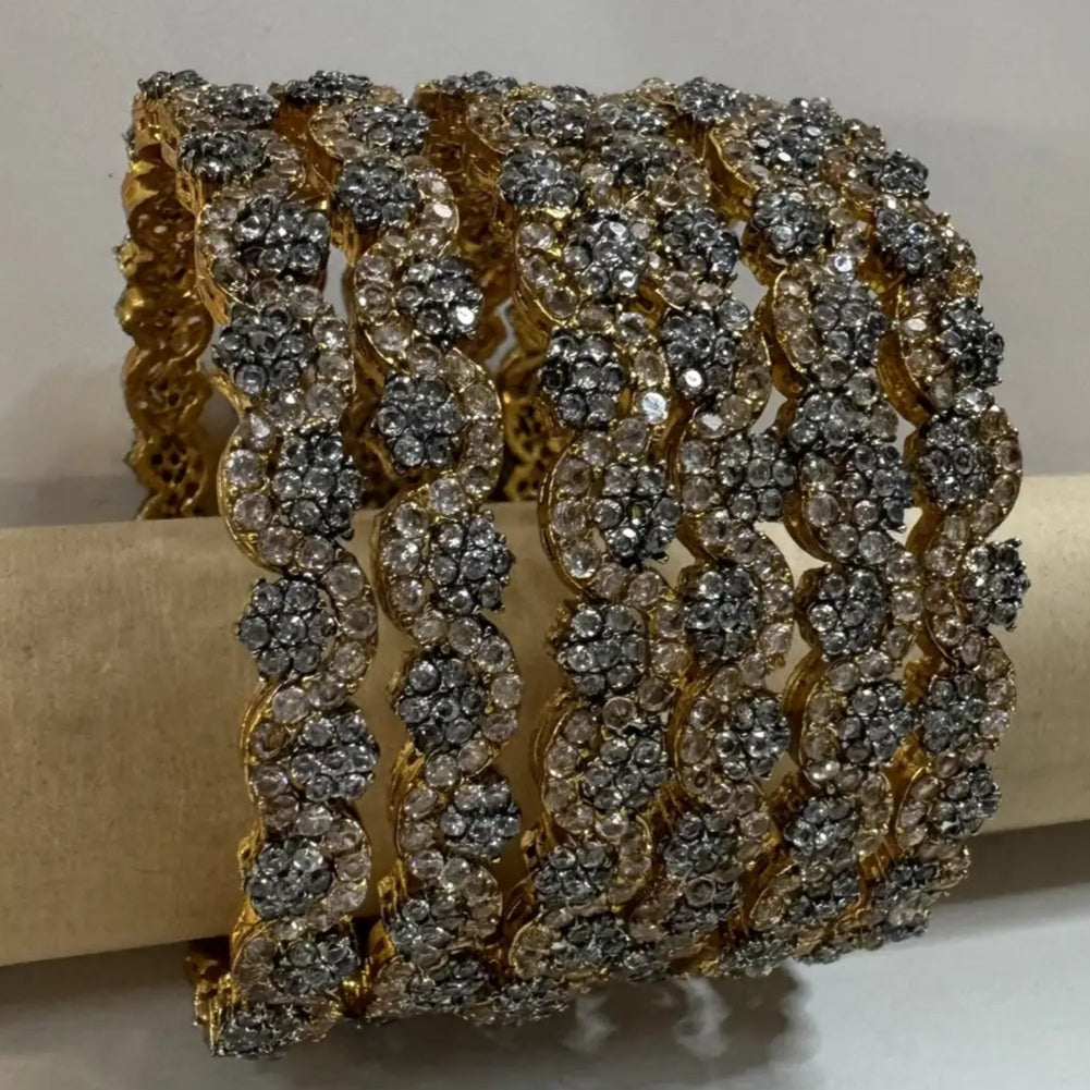 gold plated bangles with floral patterns with silver embellishments on a white background and wooden stick