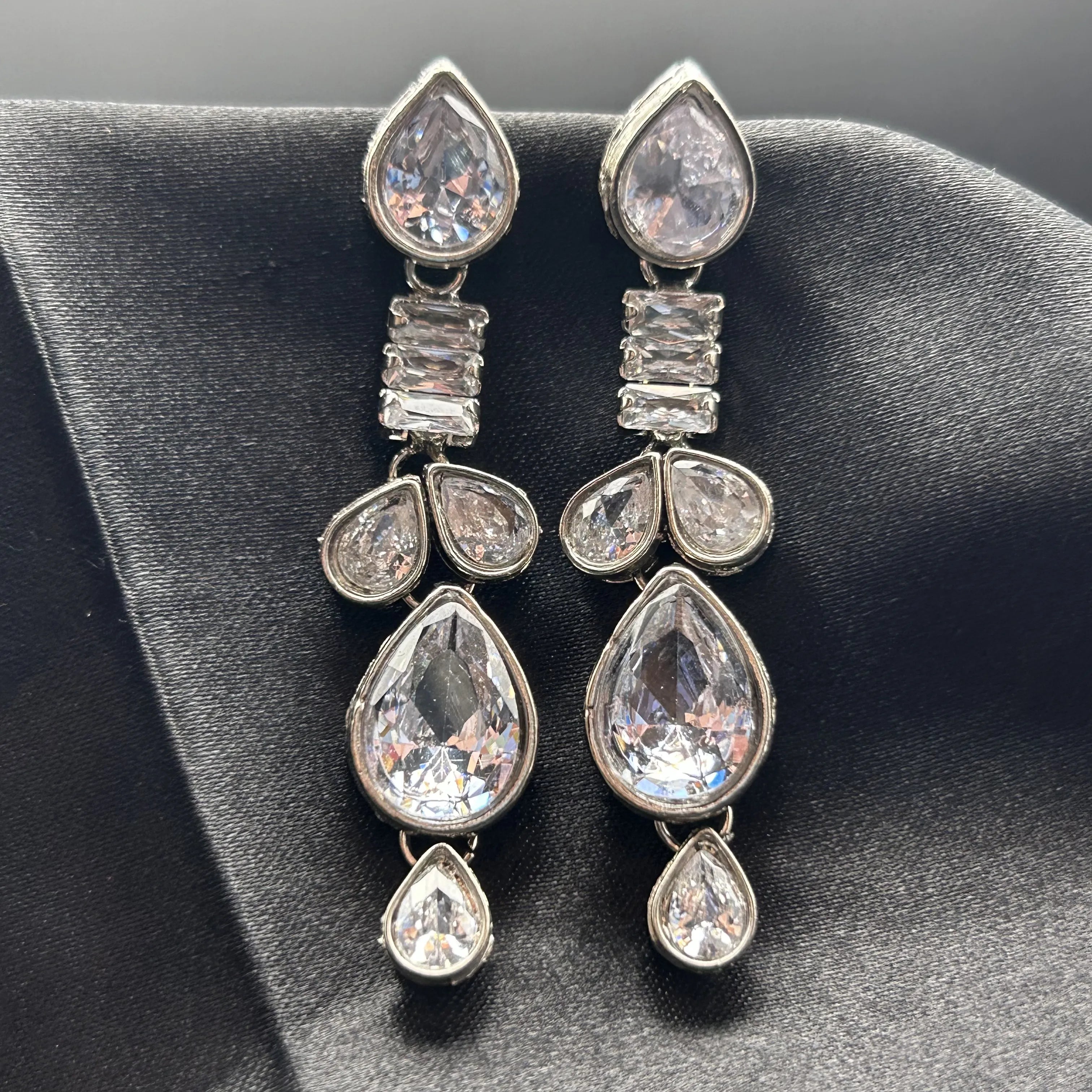 Pair of silver teardrop earrings with clear gemstones and American diamonds on a black background
