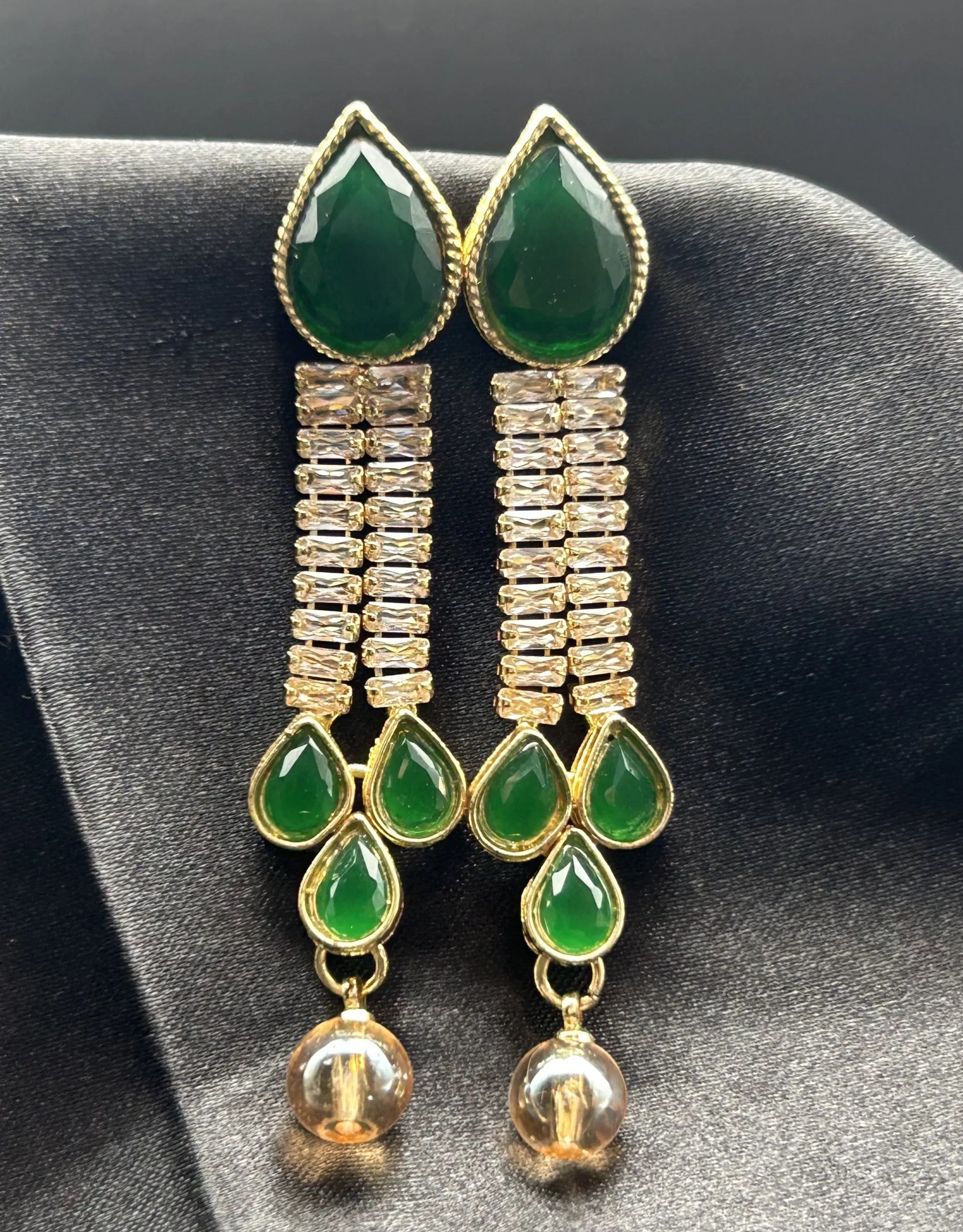 Green teardrop gold-plated earrings with gold accents on a dark fabric background