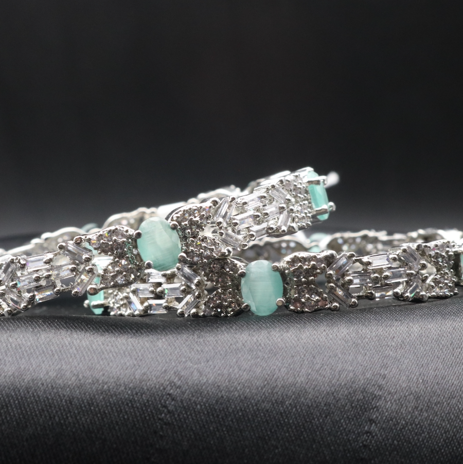 Stainless steel bangles adorned with sparkling American diamonds, and teal gemstones displayed against a dark background.