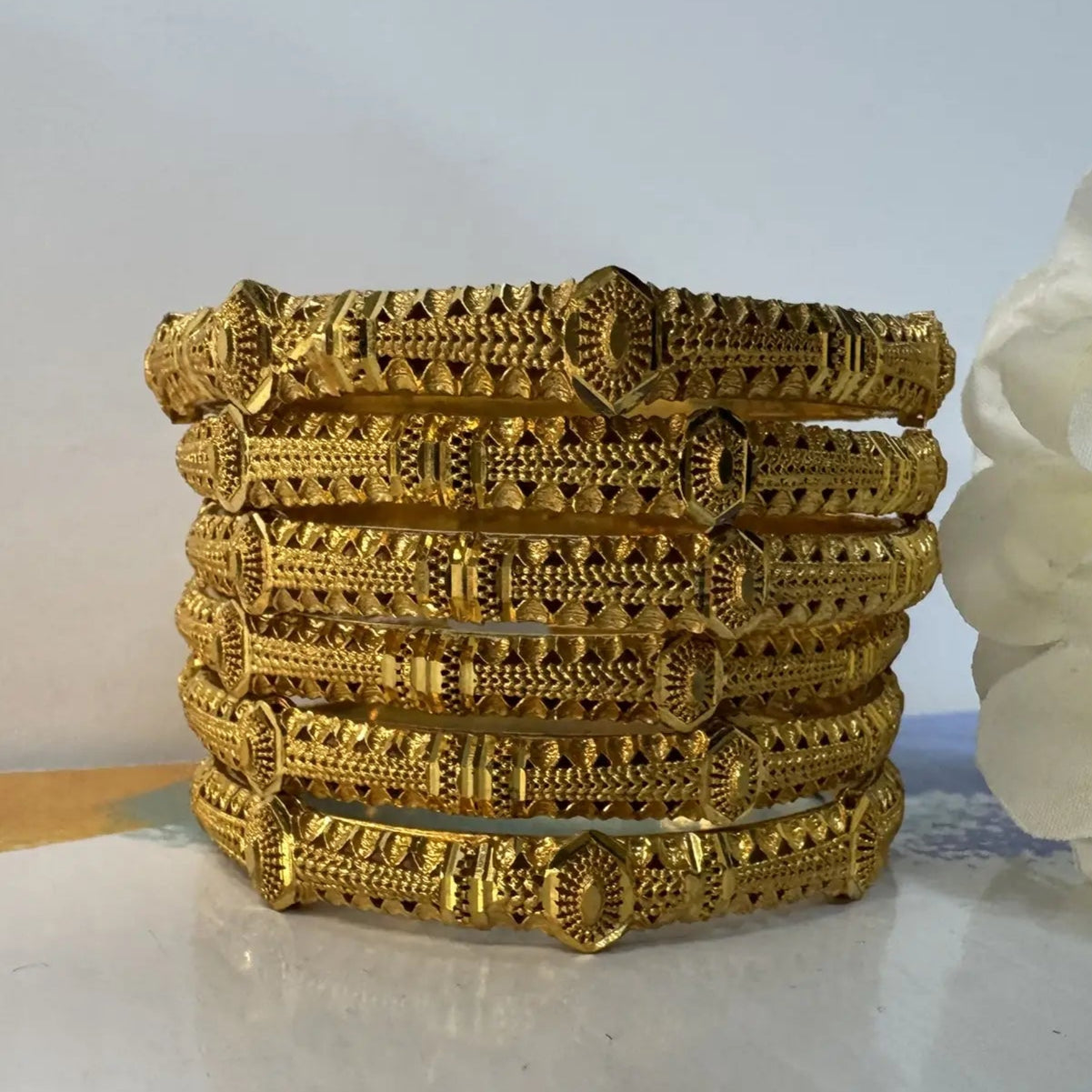 Set of 22k gold plated bangles stacked on a marble surface with a white flower in the background