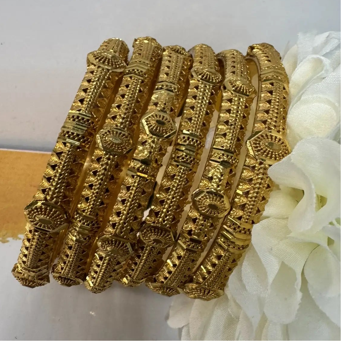 Set of 22k gold plated bangles on a white surface with a white flower