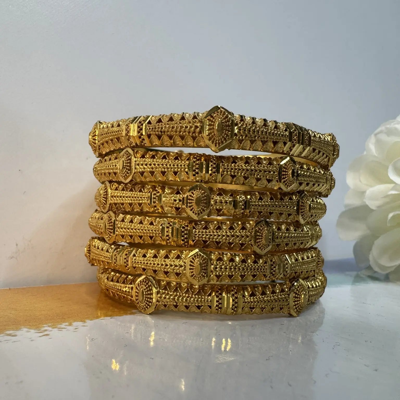 Set of gold bangles stacked on a white surface with a light gray background