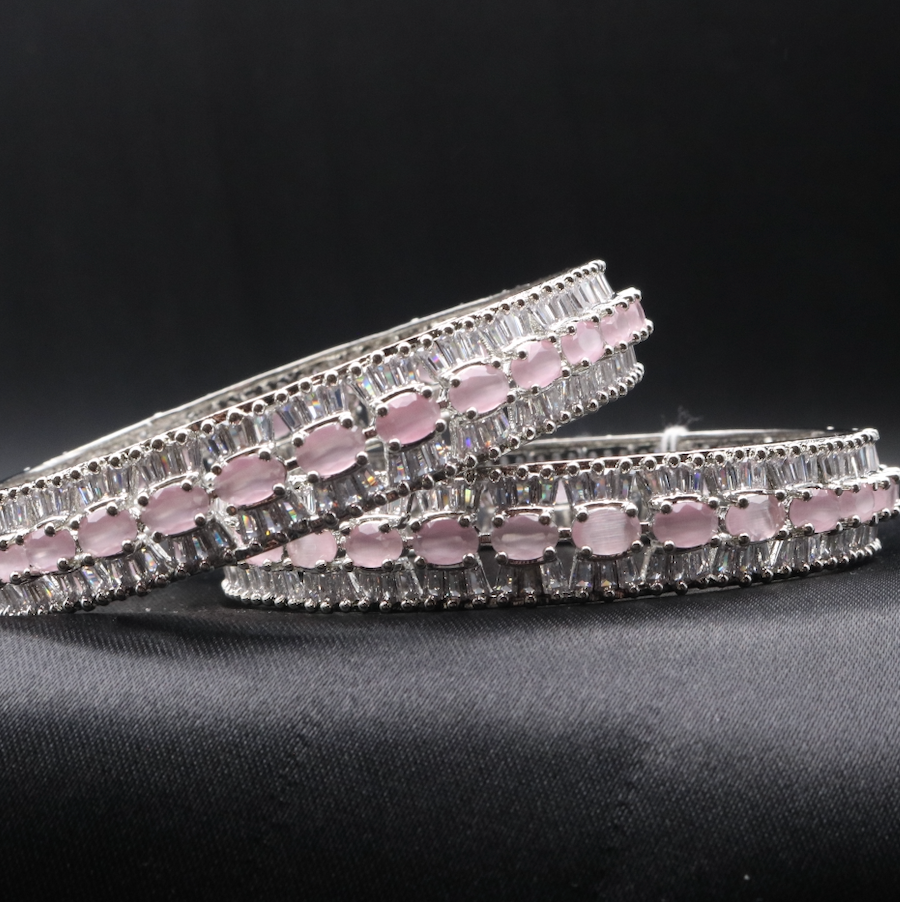 A set of stainless steel bangles adorned with sparkling American diamonds and pink gemstones, displayed against a dark background.