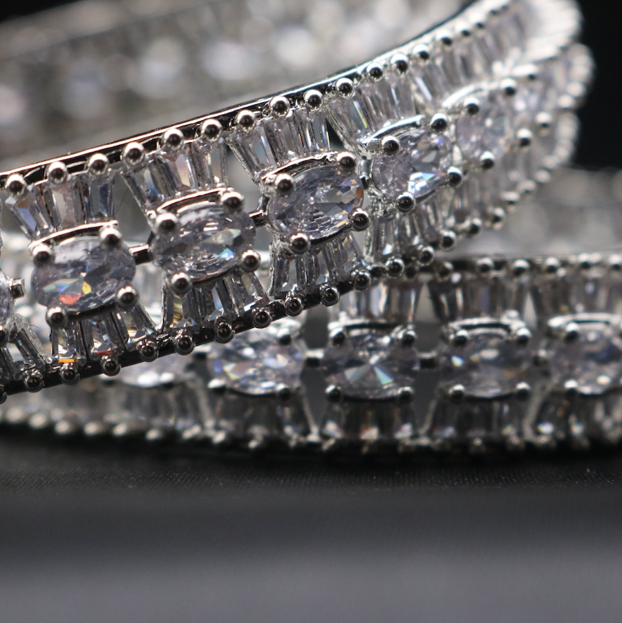 A set of stainless steel bangles adorned with sparkling American diamonds and clear gemstones, displayed against a dark background.