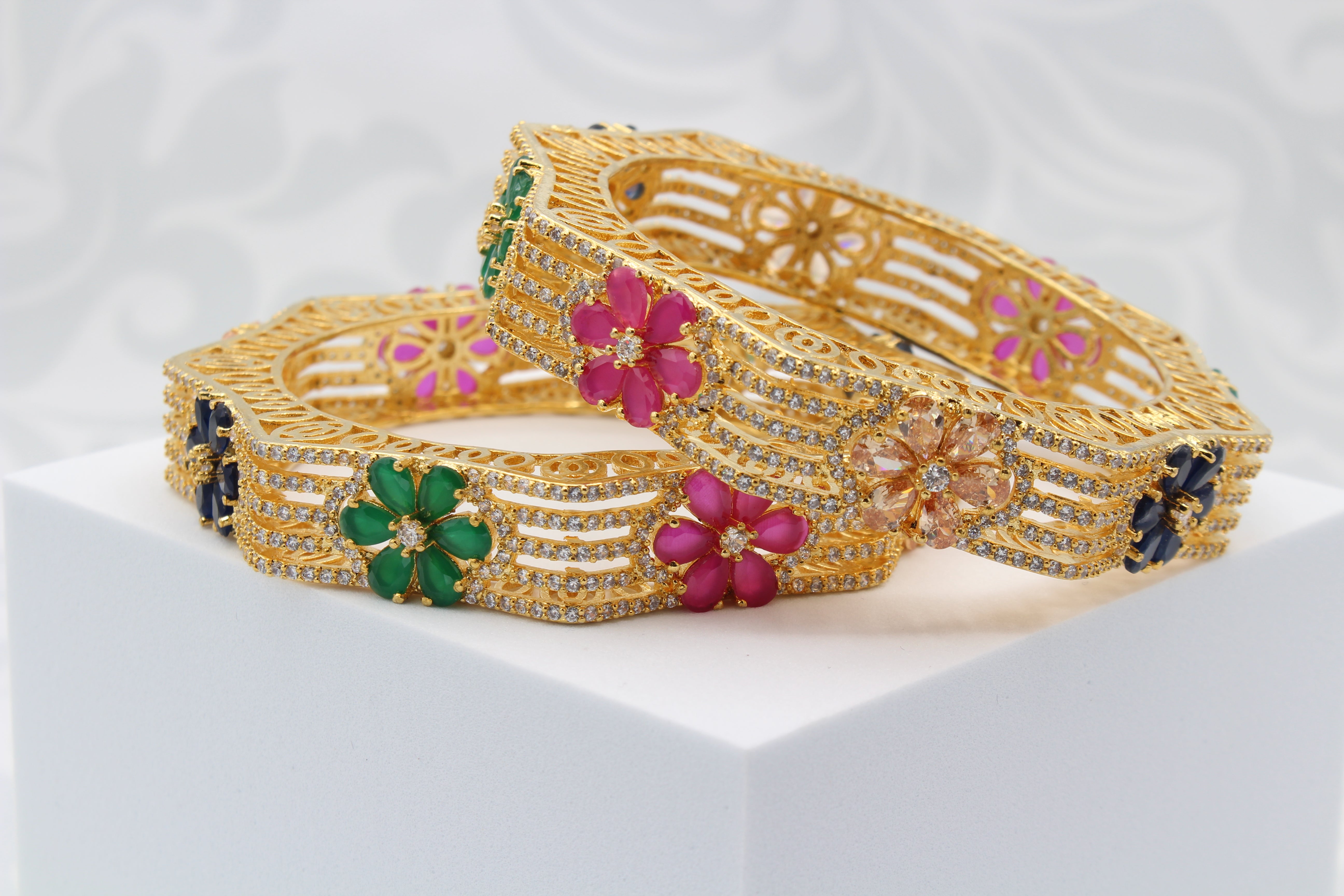 gold-plated bangles with multicolor gemstones in a hexagonal design on  white surface