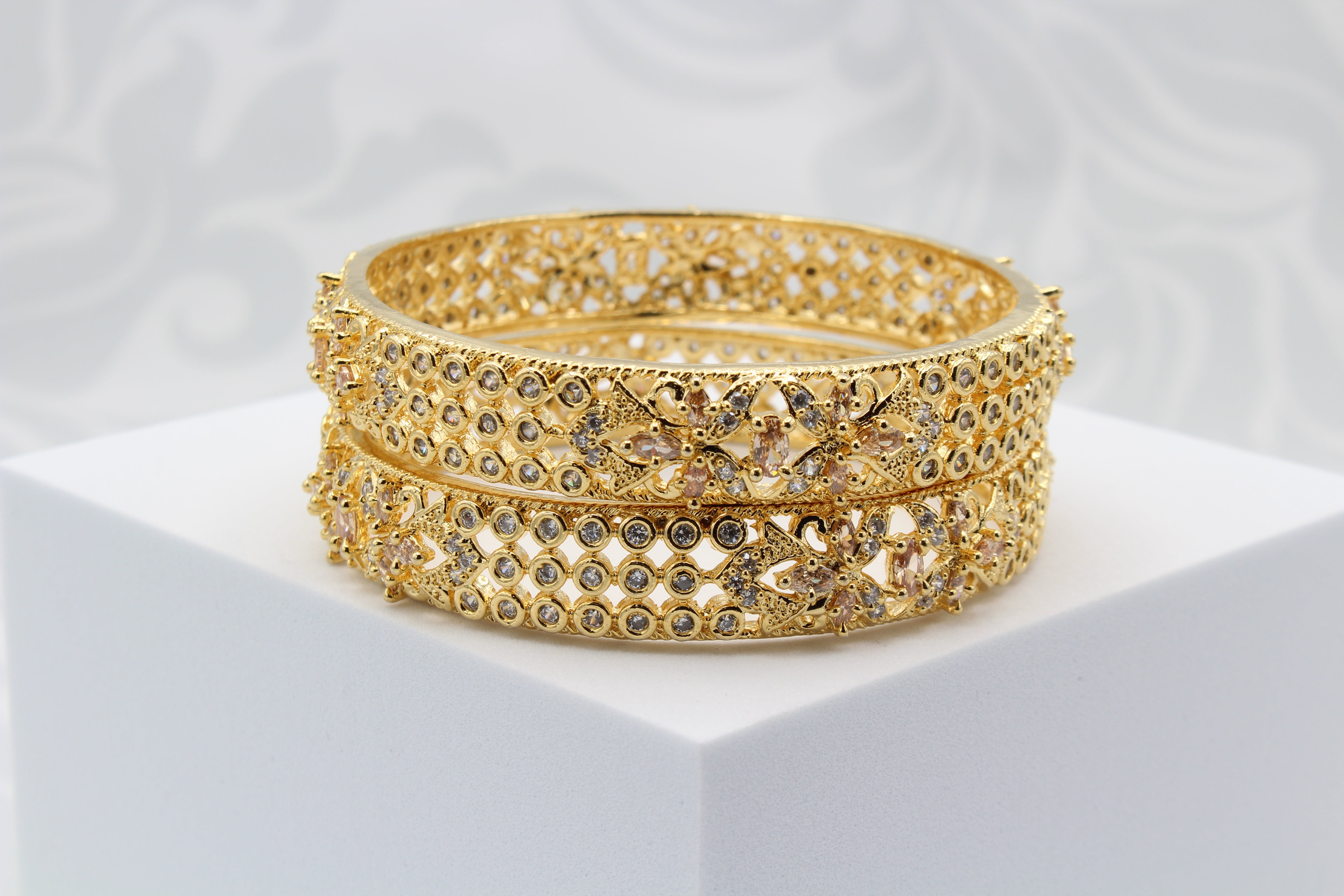 Gold plated pair of bangles with shimmering shine and intricate design on a white surface