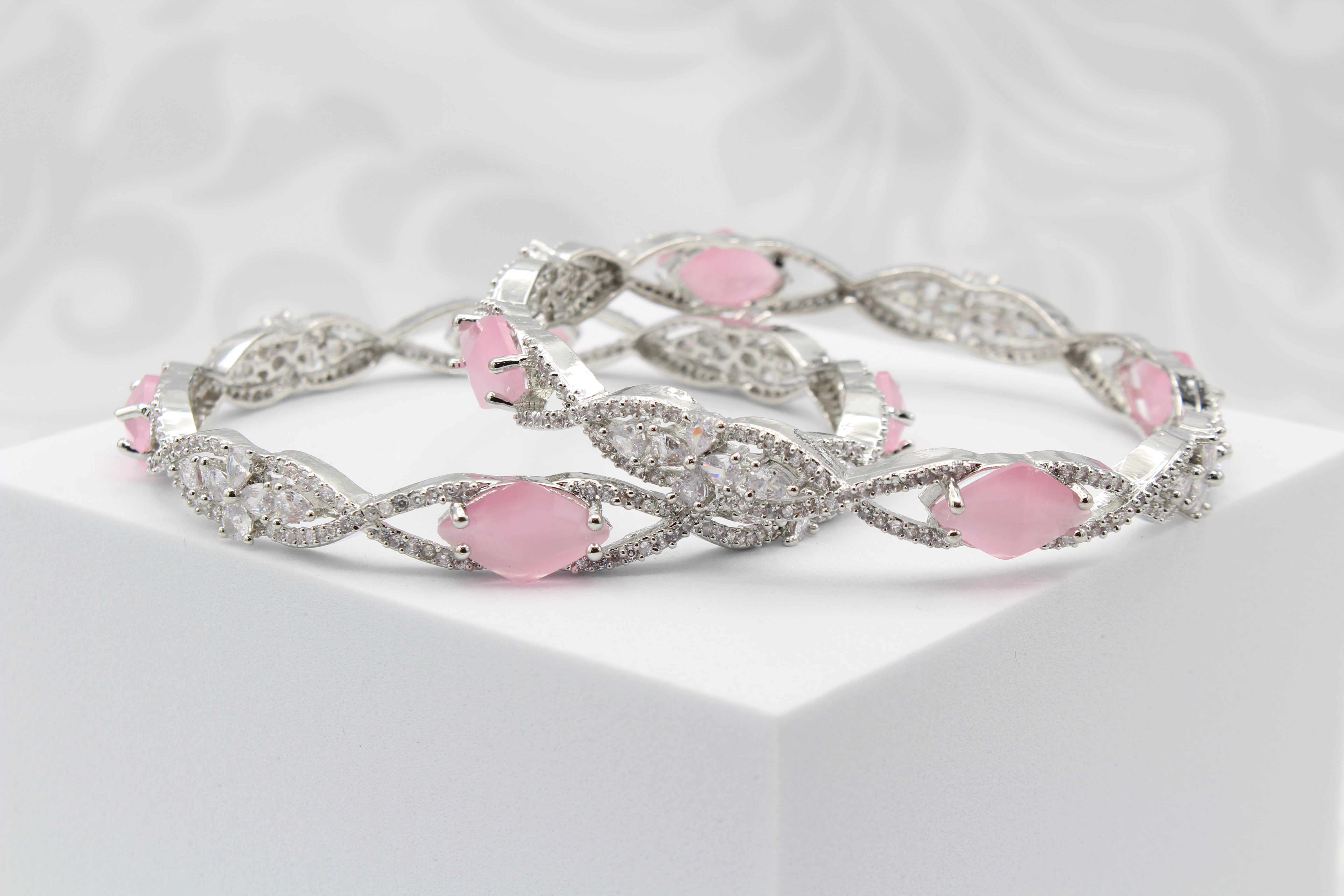 A pair of silver bangles adorned with pink rhinestones and American Diamond encrusted on a silver base, displayed on a white surface.