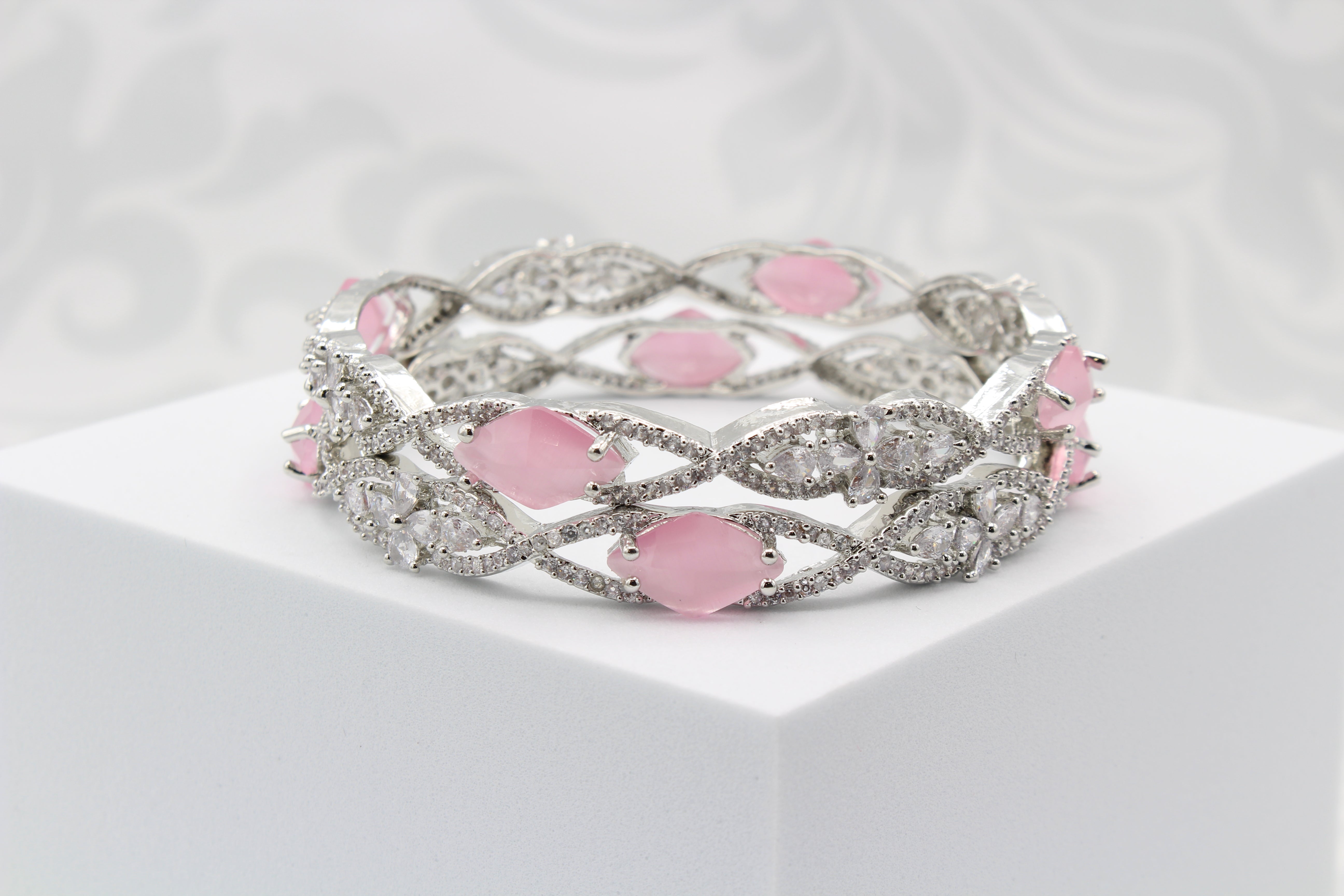 A pair of silver bangles adorned with pink rhinestones and American Diamond encrusted on a silver base, displayed on a white surface and white background